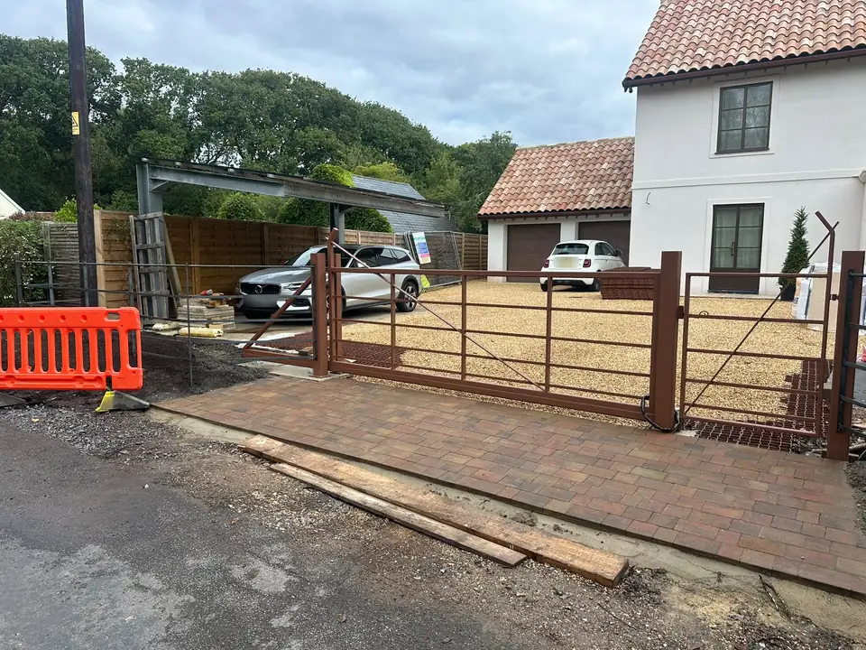 Wide driveway gate and matching pedestrian gate on square steel posts at the entrance to a new-build house, photographed during installation