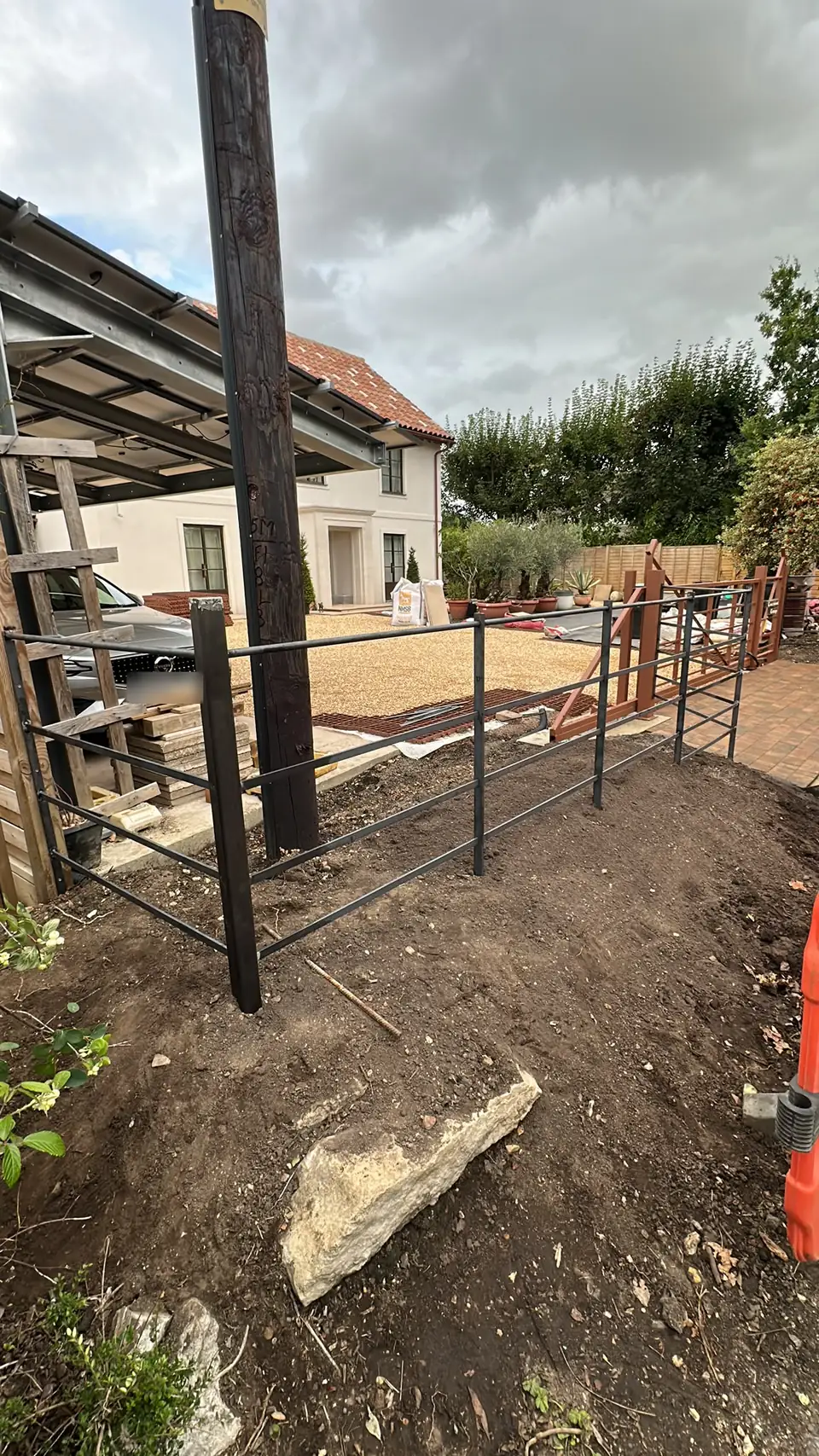 Dark steel estate railing being installed along the front boundary of a new-build house, beside the driveway gates